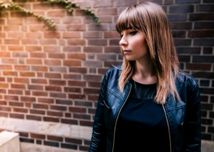woman wearing black jacket standing beside concrete brick wall photo