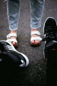 pair of black adiads shoes across person wearing white-and-brown flatbed sandals photo