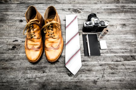 pair of brown leather boots beside necktie next to pen, notebook, and MILC camera
