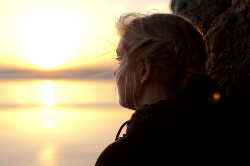 woman in black hoodie staring at the sea at sunset