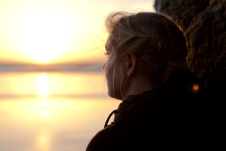 woman in black hoodie staring at the sea at sunset photo