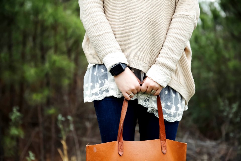 woman standing holding a brown leather tote bag