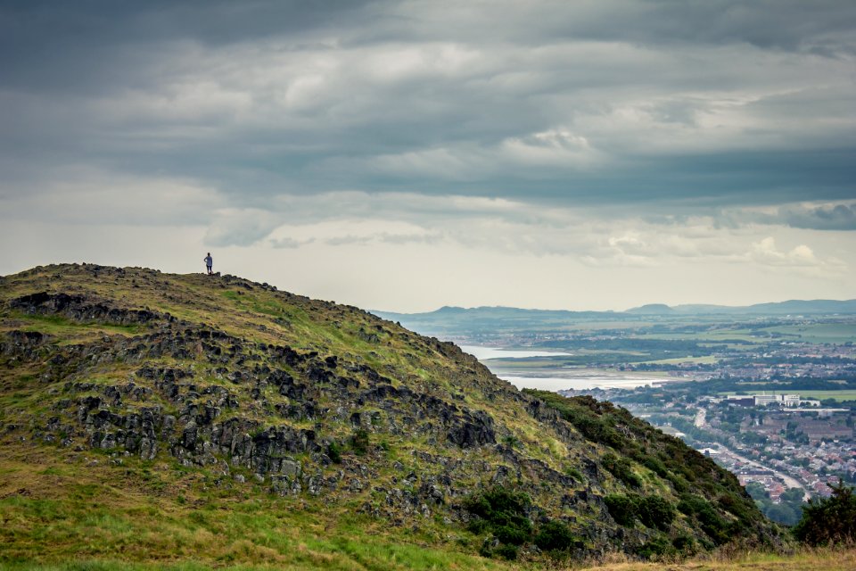 photography of person on mountain top with clouds as background