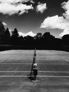 A look down the middle of a tennis net with a darkened background on a partially cloudy day. photo