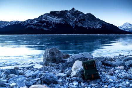 green and brown backpack leaning on stone near body of water photo