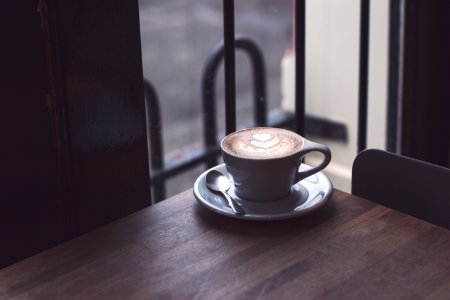 cappuccino in white teacup on brown wooden surface photo