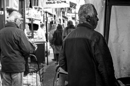 man in black jacket standing near people walking on street in grayscale photography photo