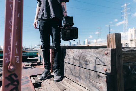 man holding black video camera while standing on plank photo