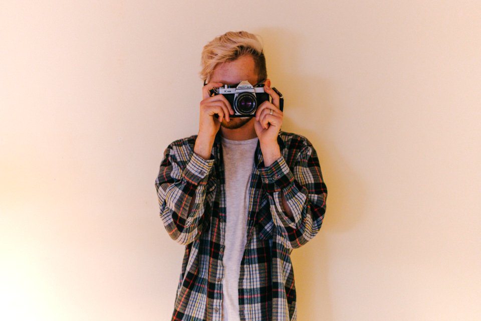 man wearing black, gray, and brown plaid collared button-up long-sleeved shirt standing while using camera