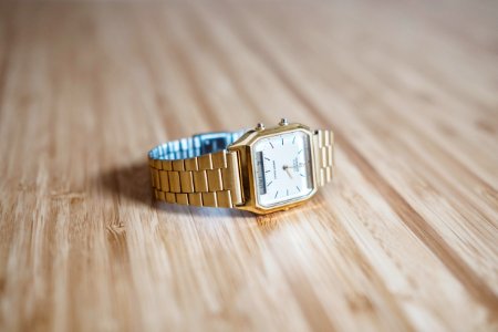 square gold-colored analog watch on brown wooden board photo