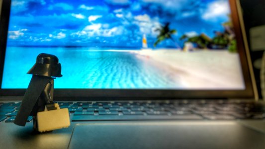 A Lego Darth Vader toy staring at a laptop screen while standing on the keyboard.