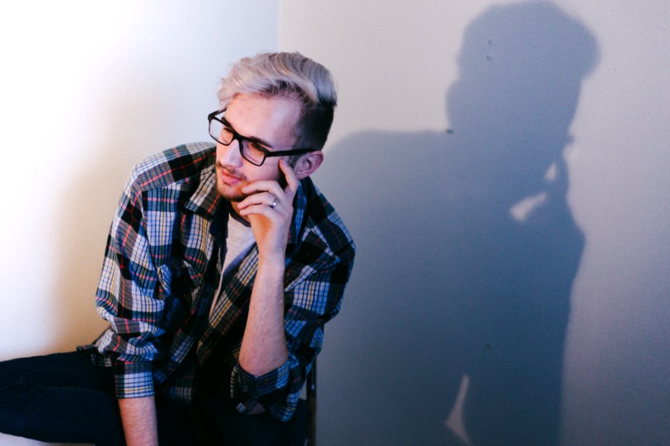 man wearing black, blue, and red plaid collared button-up long-sleeved shirt and eyeglasses sitting and putting left hand on his face photo