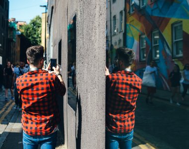 shallow focus photo of person in red and black plaid shirt holding black smartphone photo