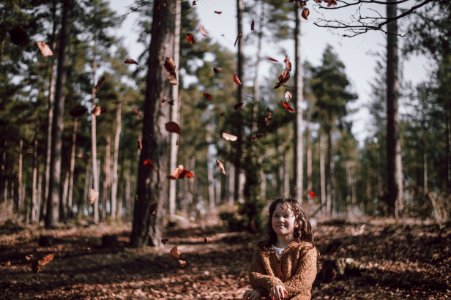 girl wearing brown jacket looking at leaves flying at daytime photo