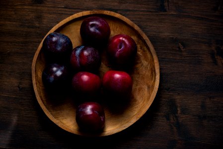 red plum fruits on round brown wooden plate photo