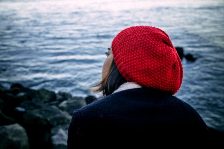 woman in black jacket and red knit cap standing on rocky shore during daytime