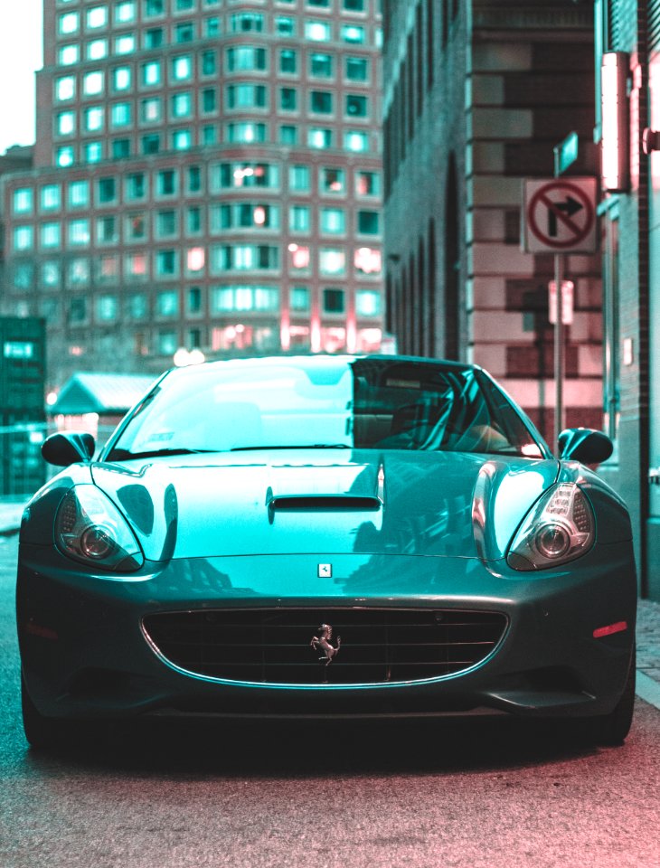 A bluish green car parked next to a building.