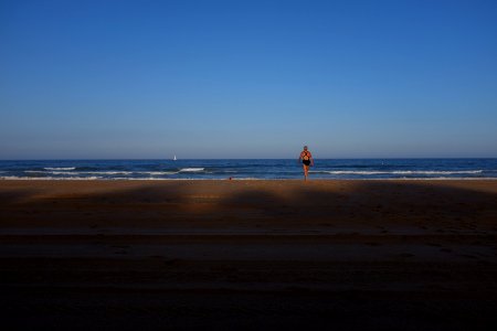 woman in black one-piece swimsuit facing blue wavy ocean under clear blue sky photo