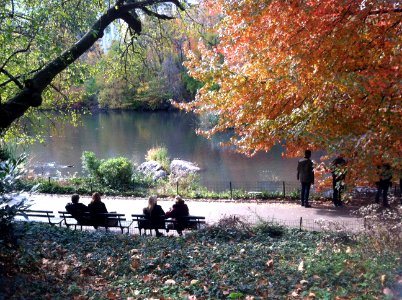 People sitting on benches and standing near a fence at a lake. photo