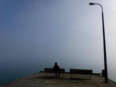 A large street light above a person sitting on one of two park benches.
