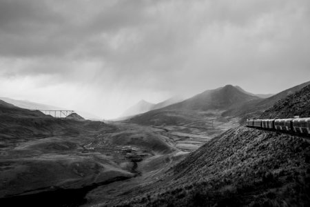 grayscale photo of train beside of mountain during cloudy sky