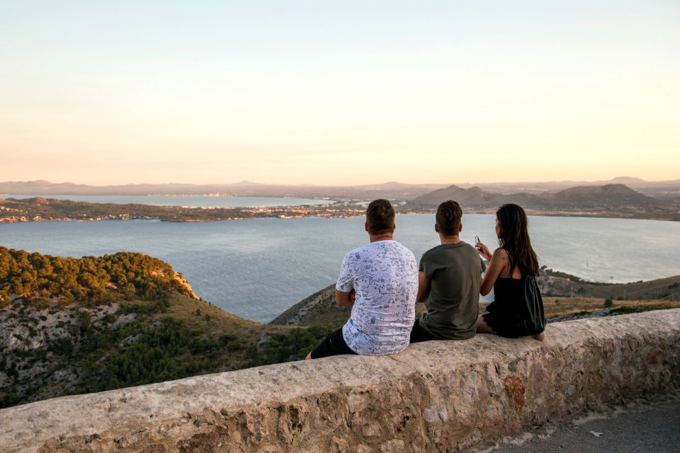 man and woman sitting on rock formation looking at the sea during daytime
