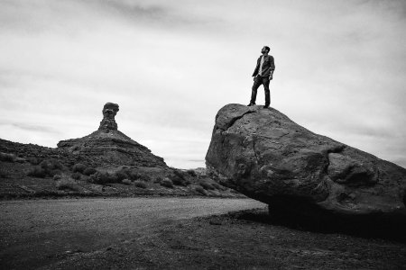 grayscale photo of man standing on rock formation photo