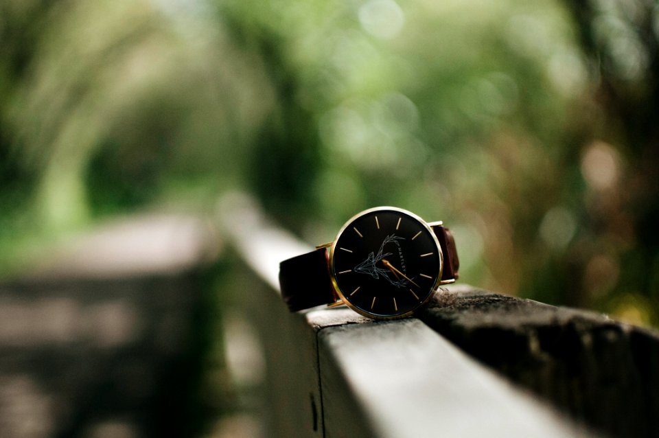 round silver-colored watch with black leather band on handrail