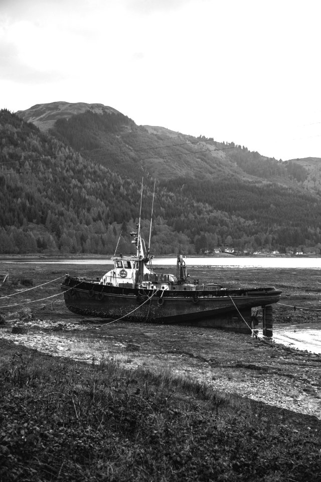 grayscale photo of boat on sea near mountain photo