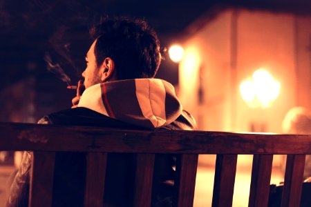 Shallow Focus Photography of Man Sitting on Bench While Smoking