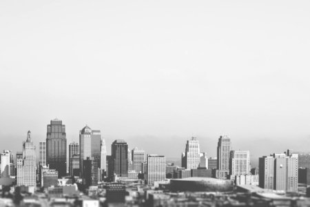 This black and white picture shows the downtown and business district of a typical american city. Some medium sized sky scrapers, some low-rise buildings and a stadium are visible. The background seems to be foggy. photo