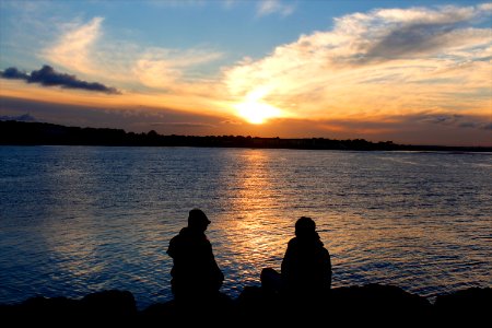 Silhouette of People Sitting on Rock Near Body of Water during Golden Hour photo