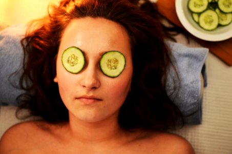 Woman Lying on White Textile With Sliced Cucumbers on Her Eyes photo