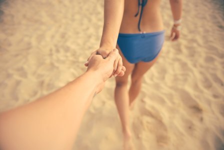 Woman Holding Man's Hand While Walking on Brown Sand