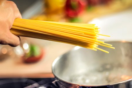 Person Holding Raw Pastas Aiming at Boiling Water in Pot photo