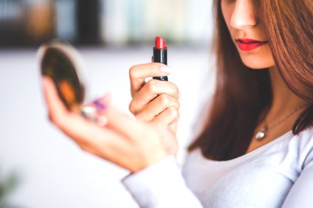 Woman with brown hair doing lipstick and holding little mirror photo