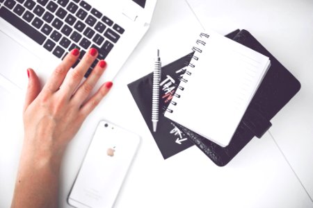 White laptop, female hand, note, pen, phone, desk