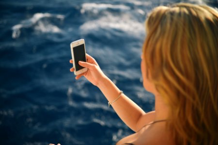 Woman Holding Silver Iphone 5s in Black Screen Near Body of Water photo