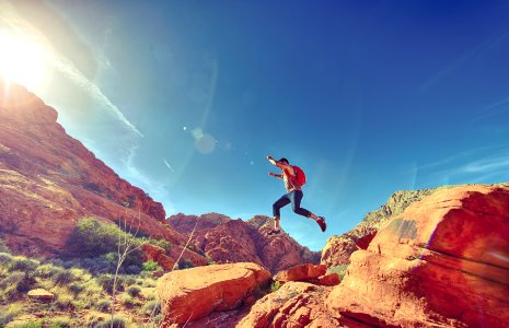 Man Jumping on Rock Formation Under Blue Sky photo