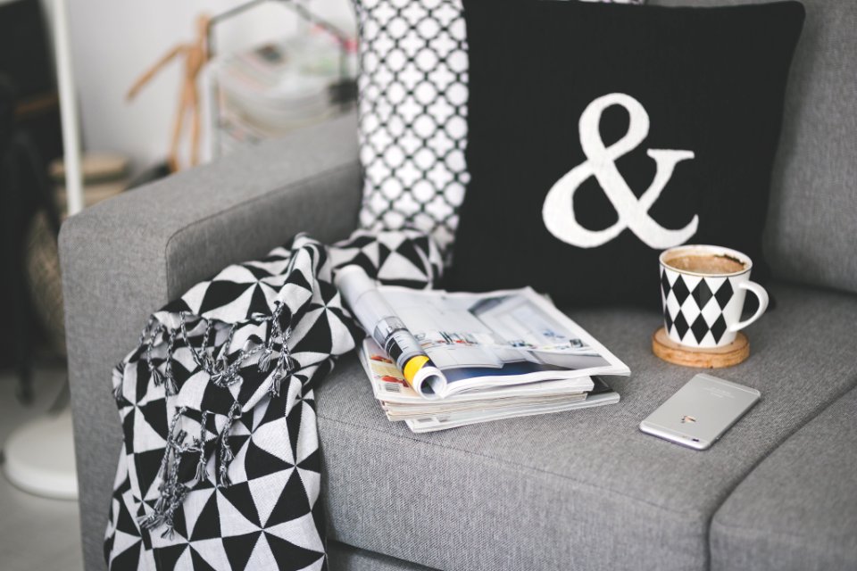 White mobile phone lying on a couch with cup and stack of magazines