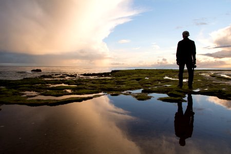 Silhouette of Man Standing on Rock Formation Near Body of Water during Golden Hour photo