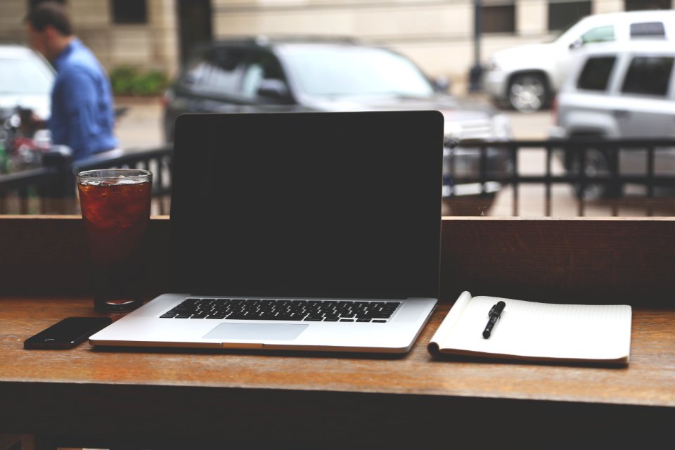 Macbook Pro With Black Screen Beside Notebook on Brown Wooden Table
