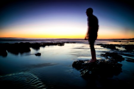 Silhouette of Man Standing on Rock Surrounded by Body of Water