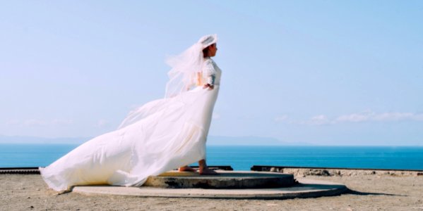 Woman in White Bridal Gown Standing in Brown Round Concrete Surface Under Blue Sky during Day Time photo