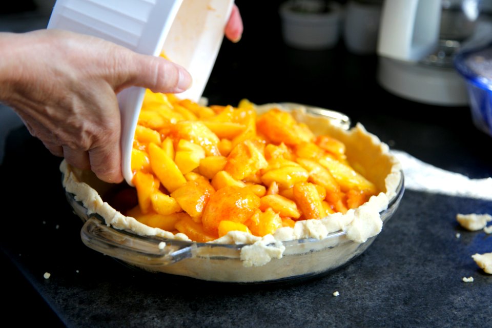 Person Pouring Cooked Food from Ramekin to Pie Tray on Gray Surface