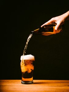 Person Pouring Yellow Liquid on Pilsner Glass Placed on Table photo