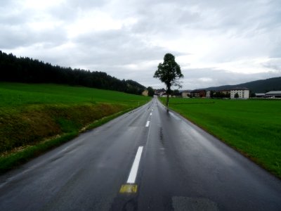 Longue ligne droite trempée, ciel bas et cycliste mouillé,… 