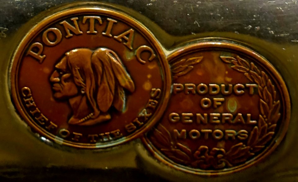 "PONTIAC_CHIEF_OF_THE_SIXES"_Native_American_art_and_"PRODUCT_OF_GENERAL_MOTORS"_hood_medallions_detail,_from-_1926_Pontiac_Two_Door_Coach_-_Automobile_Driving_Museum_-_El_Segundo,_CA_-_DSC02106_(cropped)