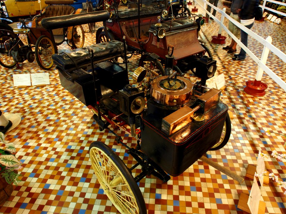 1885_De_Dion_Bouton_tricycle_with_front_mounted_boiler_and_water_tank_and_coal_chest_on_each_side_of_rear_wheel_at_the_Musée_Automobile_de_Vendée_pic-1