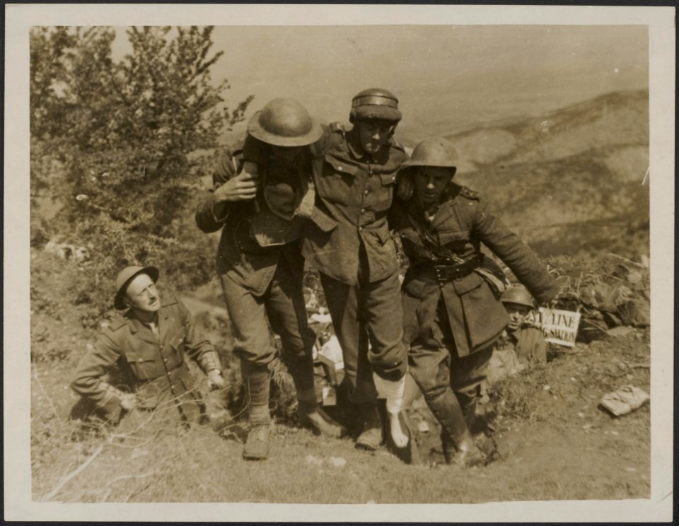 A_padre_assists_the_R.A.M.C._Royal_Army_Medical_Corps_in_lifting_a_wounded_sol,_Bestanddeelnr_158-2458